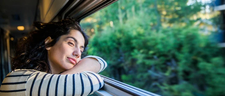 En kvinna som tittar ut från ett tågfönster ifrån ett tåg i rörelse.