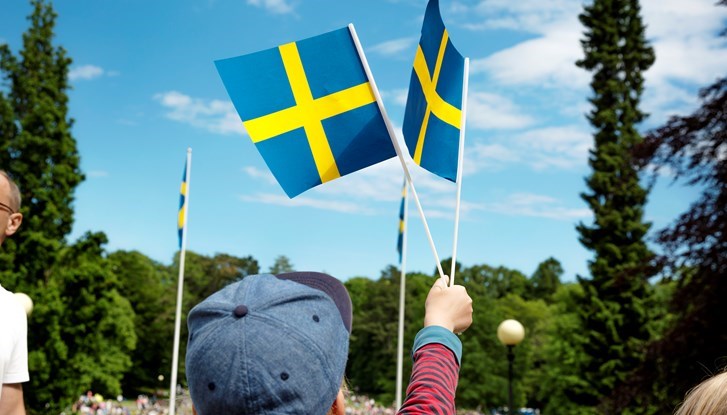 En pojke som viftar med två svenska flaggor.