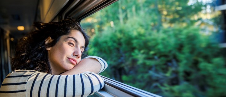 Bilden visar en kvinna som reser med tåget och lutar sig  på fönster medans hon tittar ut